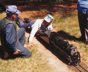 Here is a good example of "ground flying" as Carl puts it. Bob Hornsby is stopped on the mainline with his locomotive as he has a brief chart with the late Ralph Lathrop. Standing to the right is the late Ev Ryan. Bob is lying on a long flat car to keep the center of gravity low (for speed).
